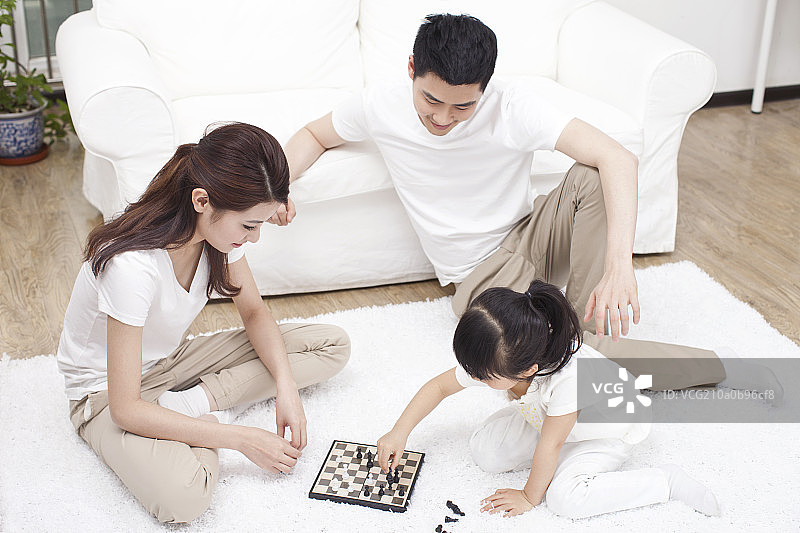 三口之家围坐在地毯上玩国际象棋图片素材