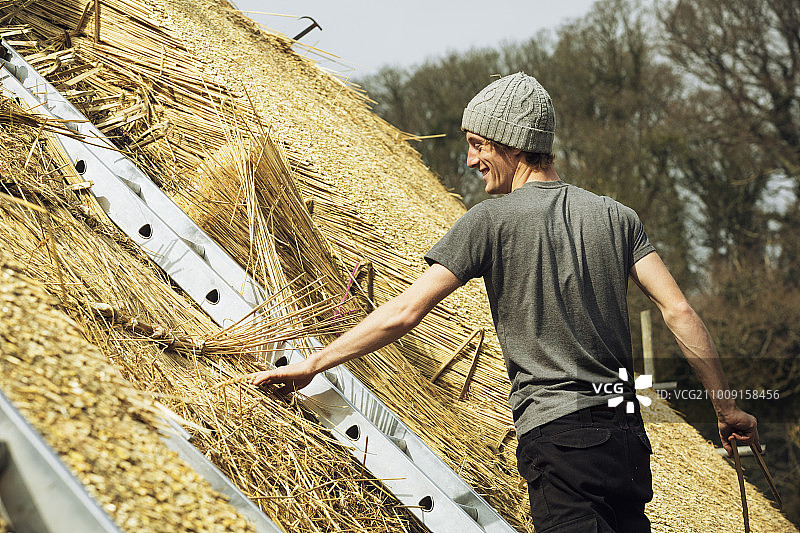 站在梯子上用茅草盖屋顶的年轻人图片素材