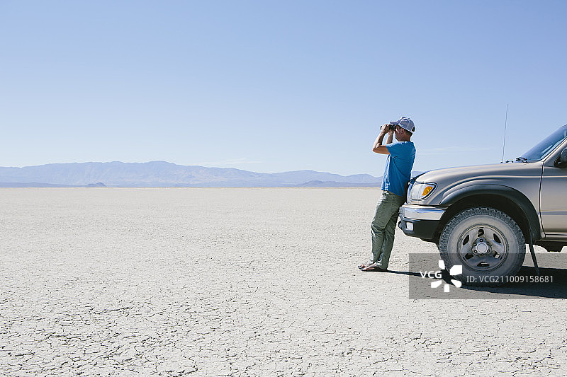 男子站在广阔的沙漠中，靠在卡车上用双筒望远镜观看，黑石沙漠图片素材