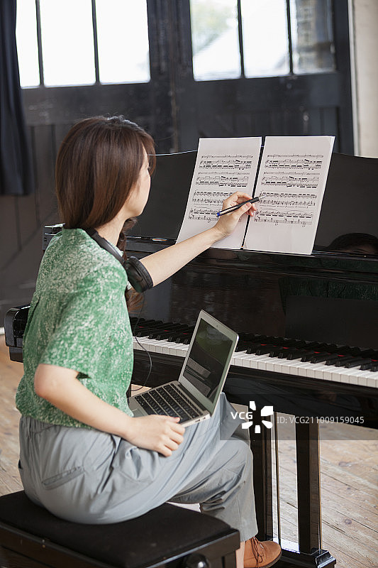 年轻女人在排练室里坐在大钢琴旁，注释乐谱图片素材