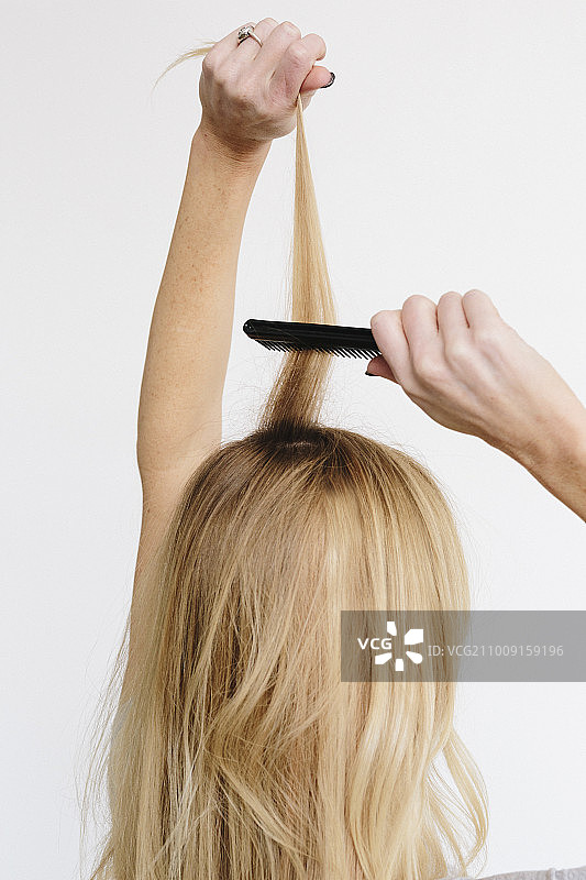 用梳子的金色波浪长发年轻女子（背面视角）图片素材