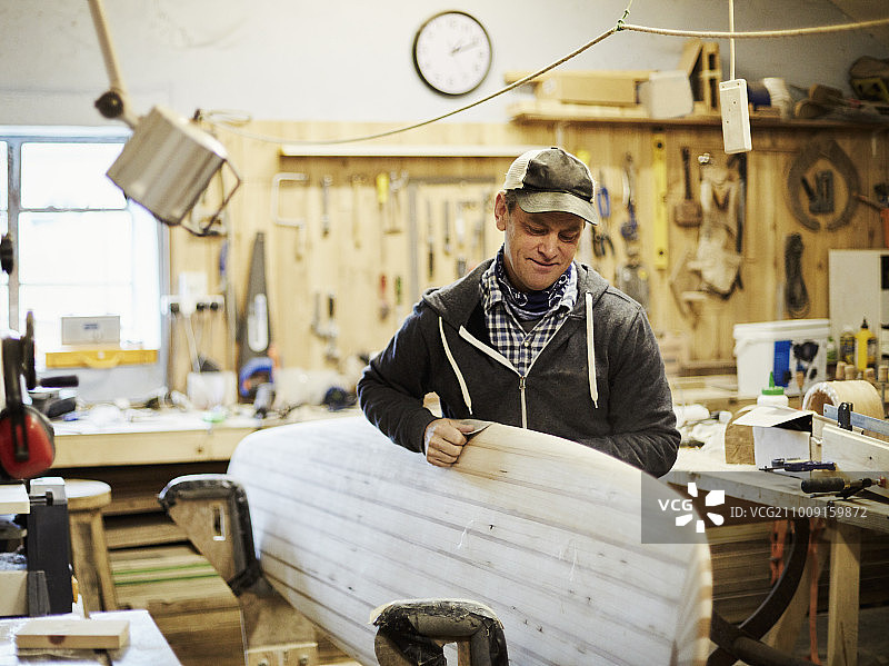 男子在工作室打磨木制冲浪板图片素材