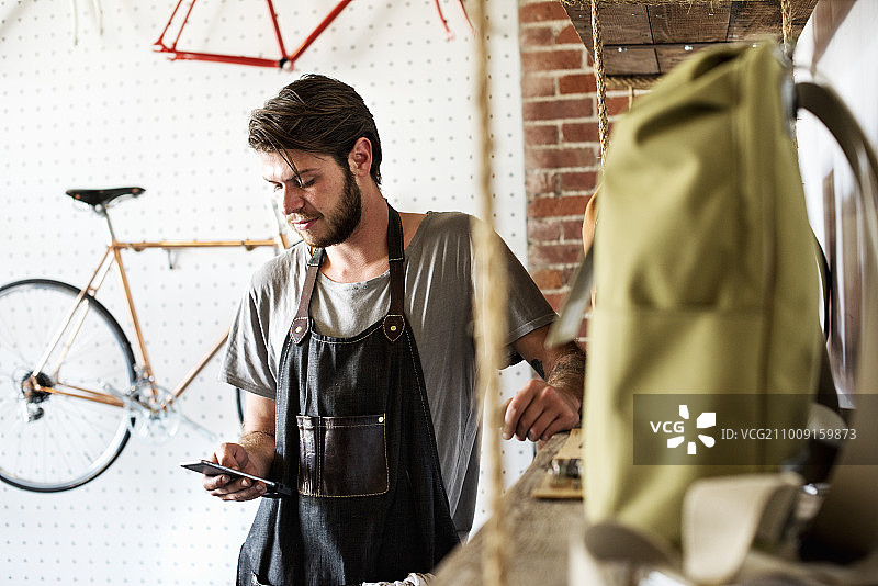 男人在自行车修理店工作并看智能手机图片素材