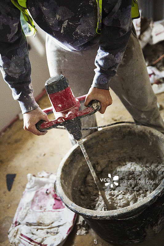 建筑工人在建筑工地用电动搅拌机在桶中搅拌石膏。图片素材