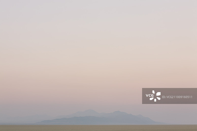 沙漠景观中，黎明时分笼罩在薄雾中的山脉图片素材