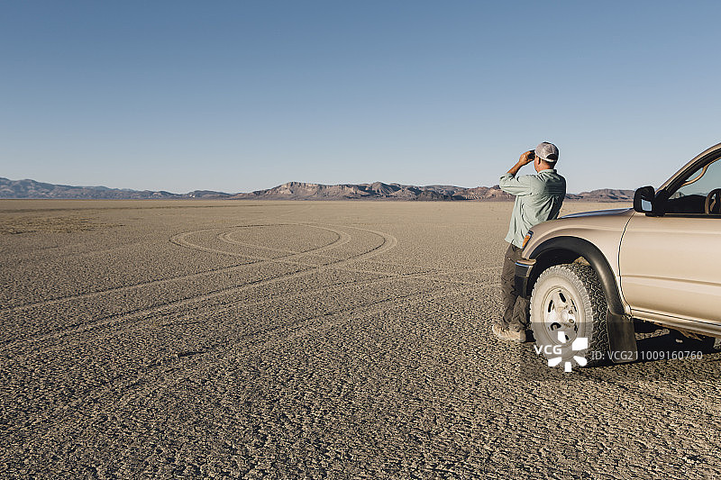 男子站在广阔的沙漠中，靠在卡车上用双筒望远镜观看，黑石沙漠图片素材