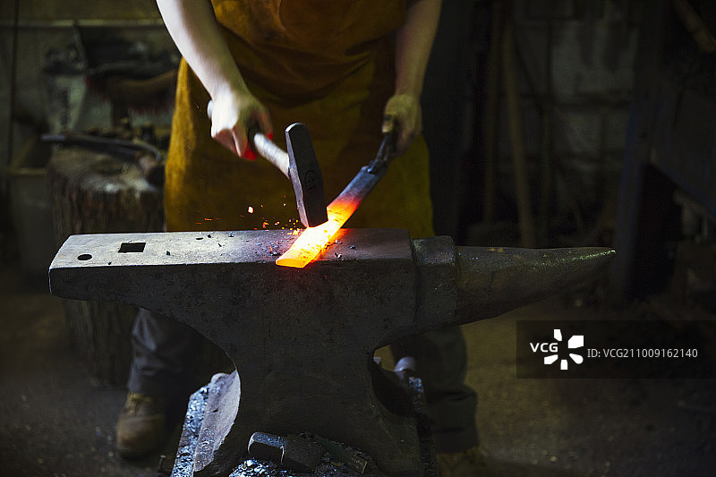 铁匠在工作坊中用锤子敲打铁砧上烧红的金属图片素材