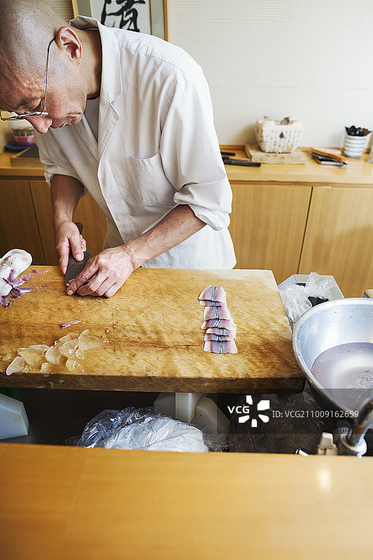 小型商用厨房里的大厨用大刀切鱼制作寿司图片素材