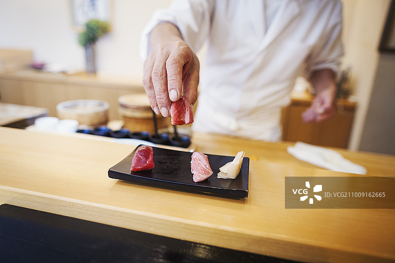 在小型商业厨房工作的厨师，一位厨师长展示一盘新鲜的寿司。图片素材