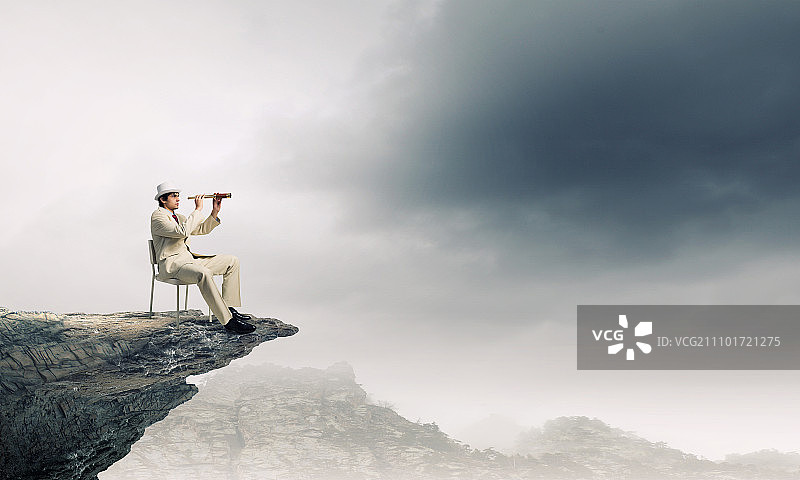 寻找未来视角。身穿白色西装、头戴帽子的商人坐在椅子上，用望远镜观察图片素材