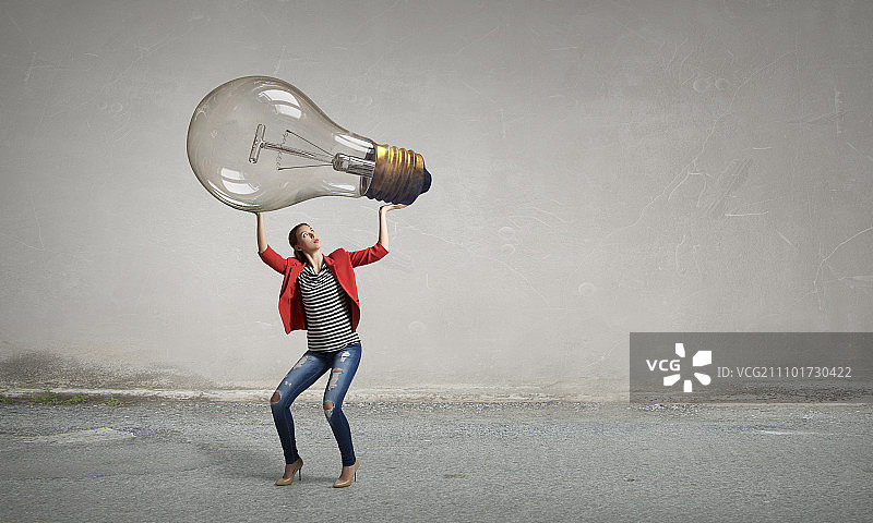 拿着大玻璃灯泡的女孩。穿着红色夹克的年轻女孩推动玻璃灯泡图片素材