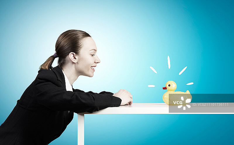 拿着鸭子玩具的女人，年轻女商人和桌子上的黄色橡皮鸭玩具图片素材