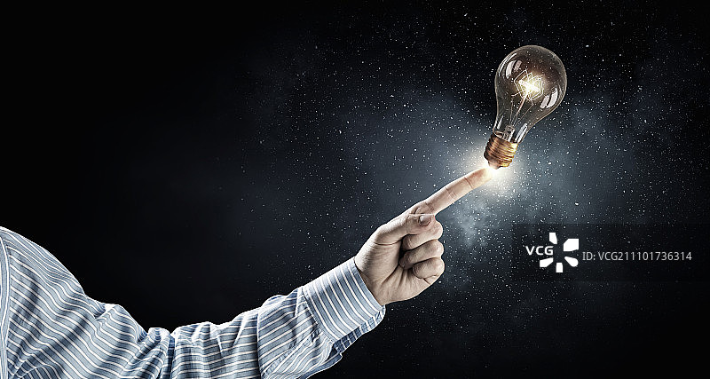 男人指着灯泡。商人指着黑暗背景中发光玻璃灯泡图片素材