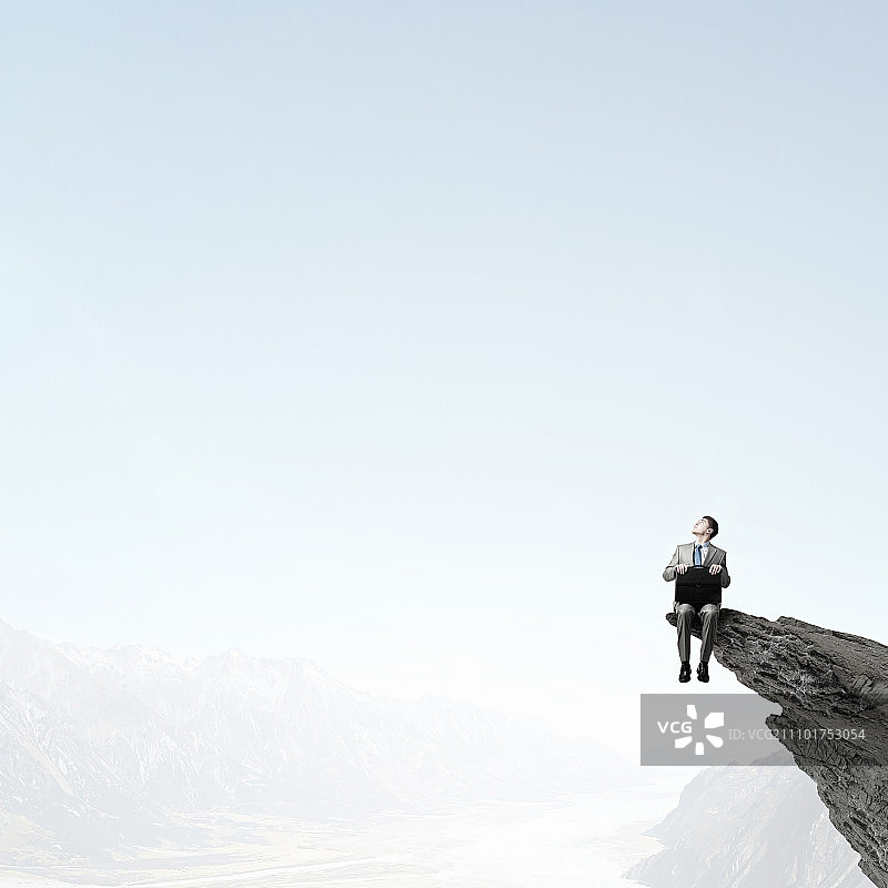 拿着公文包的商人：手持公文包坐在岩石顶部的商人图片素材
