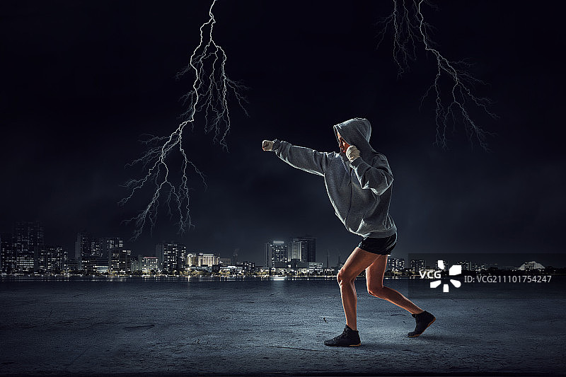 年轻女拳击手训练。年轻女拳击手站在户外，背景是城市景观图片素材