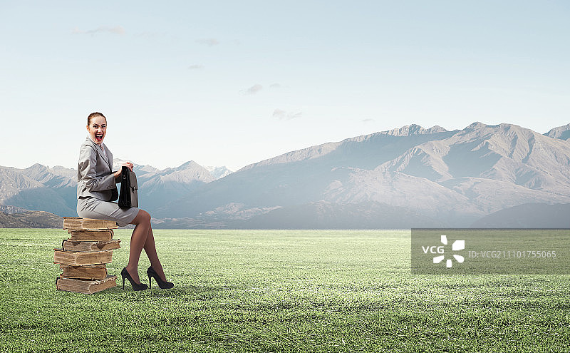 年轻女人坐在书堆上，手捧书本，从工作中稍作休息图片素材