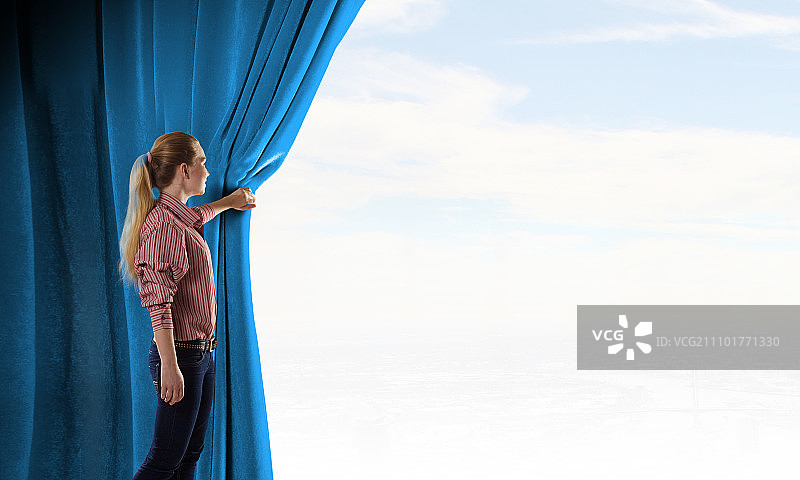 拉开窗帘的女孩。穿着休闲装的年轻女子拉开窗帘图片素材