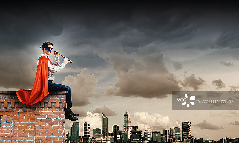 屋顶上的超人。超人穿着斗篷和面具坐在建筑物顶部图片素材