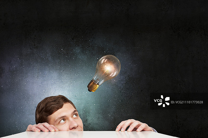 灯泡概念：从桌子下看玻璃灯泡的年轻人图片素材