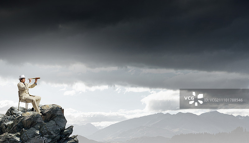寻找未来视角。身穿白色西装、头戴帽子的商人坐在椅子上，用望远镜观察图片素材