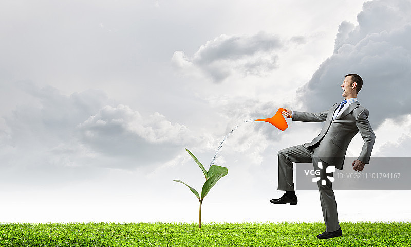 正确投资以获得收入。年轻商人用水壶给绿色植物浇水图片素材