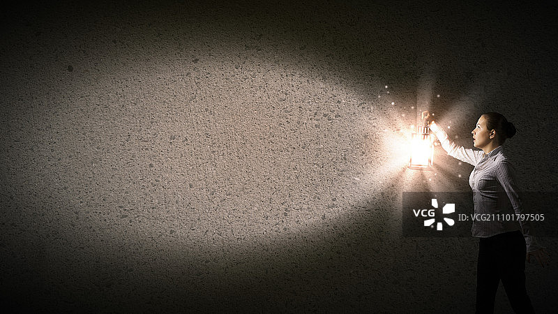 拿着灯笼的女商人：年轻女商人手提灯笼在黑暗中行走图片素材