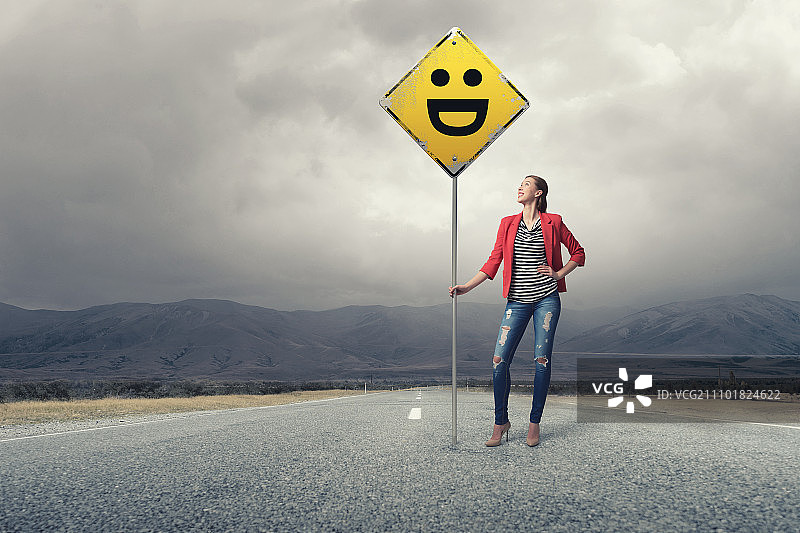 在沥青路上穿着红色外套的年轻漂亮女孩展示路标图片素材