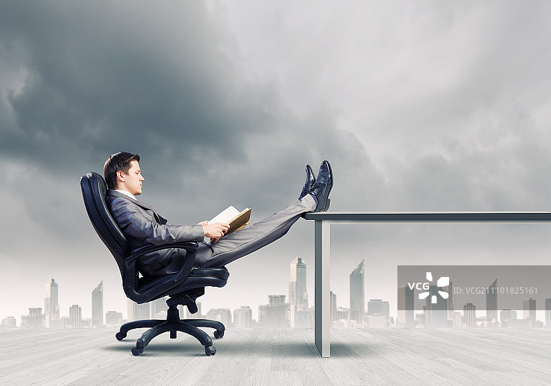 坐在椅子上的商人。手捧书本坐在椅子上的年轻商人图片素材