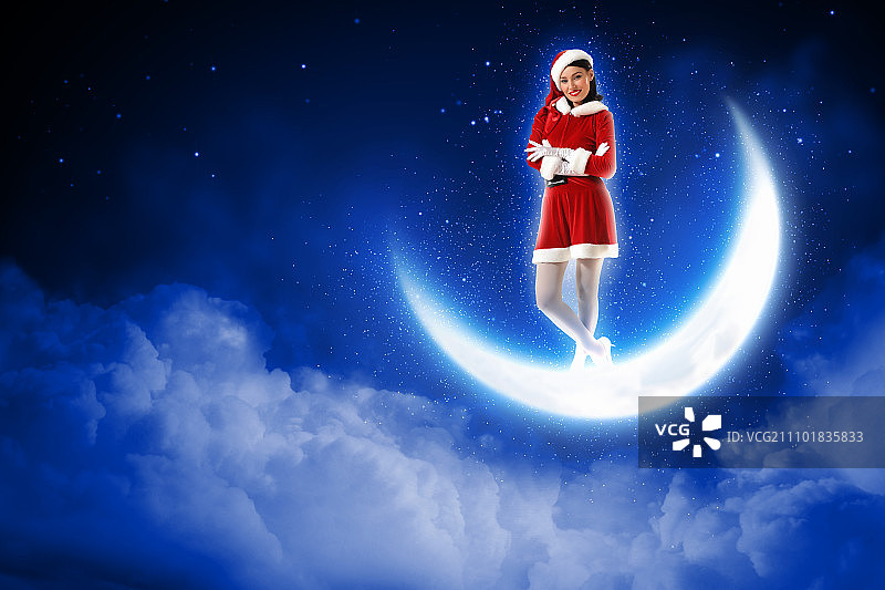 圣诞女孩坐在月亮上的照片。站在冬季森林上方闪亮月亮上的圣诞女孩照片图片素材