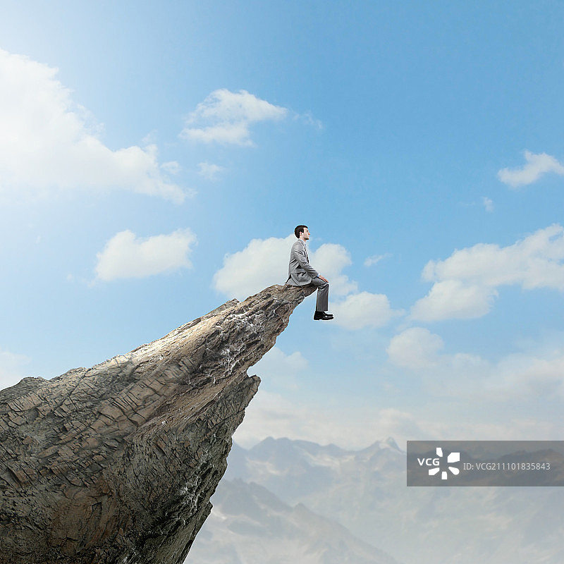 商业风险，年轻商人坐在岩石山边缘图片素材