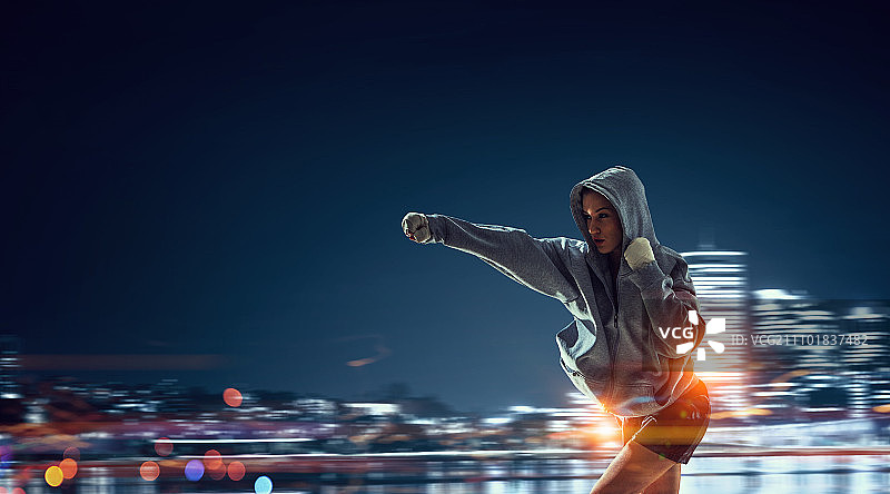 年轻女拳击手训练。年轻女拳击手站在户外，背景是城市景观图片素材