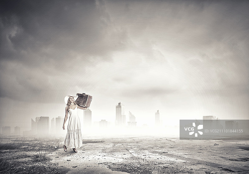 身穿白色长裙、头戴帽子的女人拉着行李箱出行图片素材