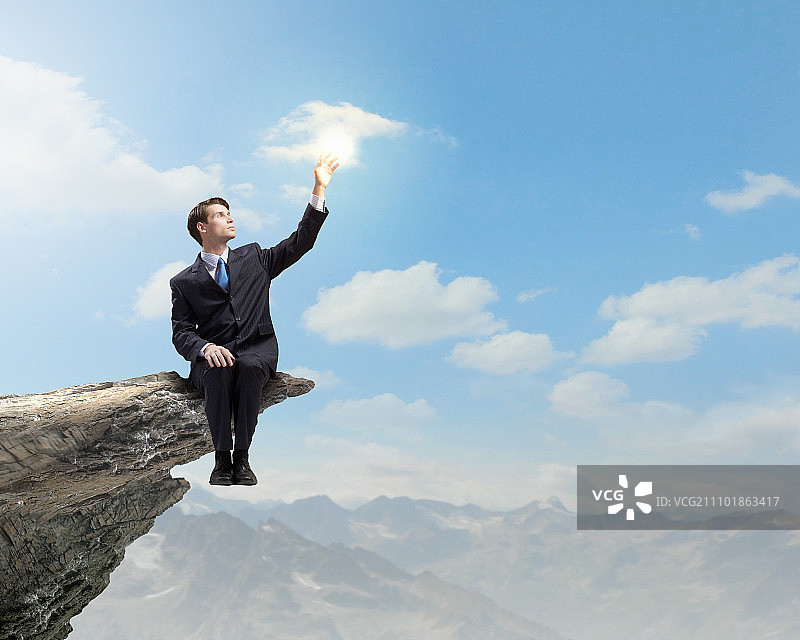 站在顶端的商人：坐在岩石边缘的年轻商人图片素材