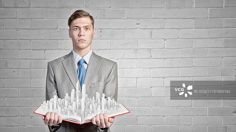 工程与建筑：商人手持打开的书籍，书页上呈现建筑模型图片素材