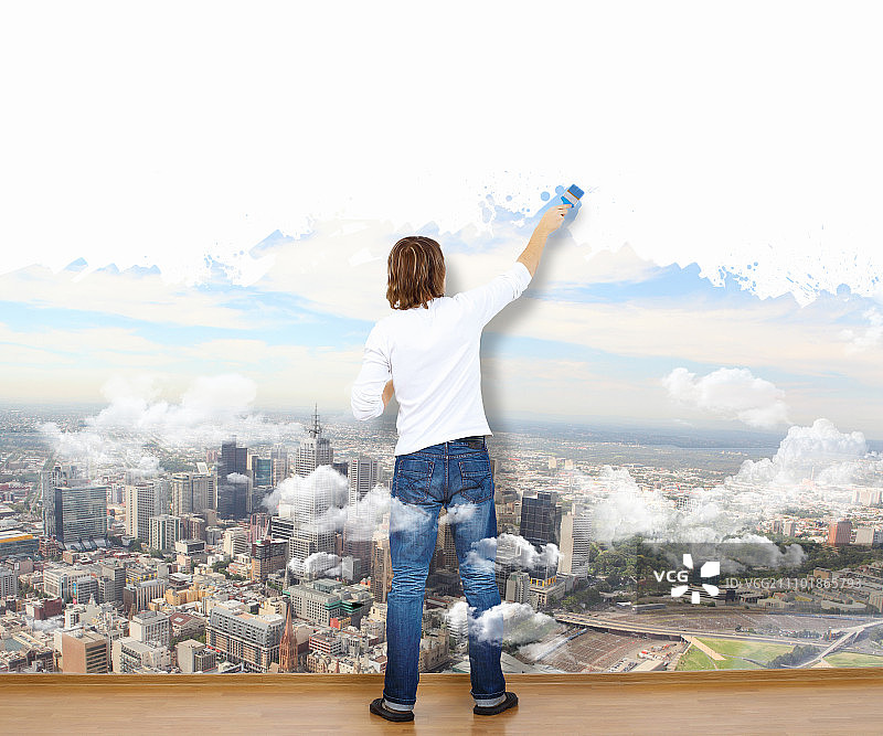 拿着画笔和绘有自然景观墙壁的年轻男人图片素材