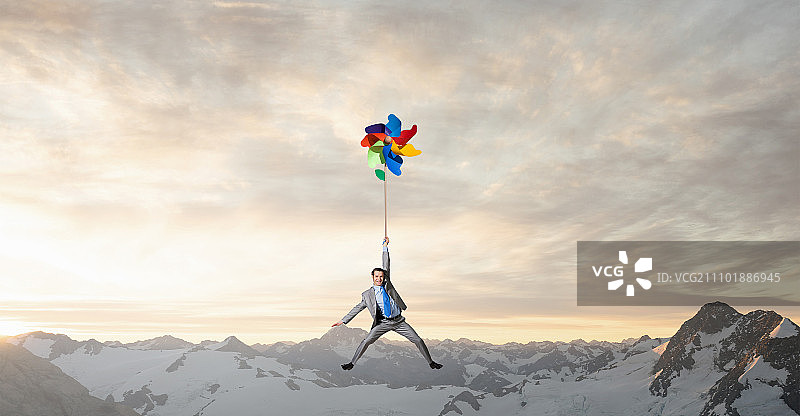 自由的好日子：年轻快乐的商人乘坐彩色风车在天空中飞翔图片素材