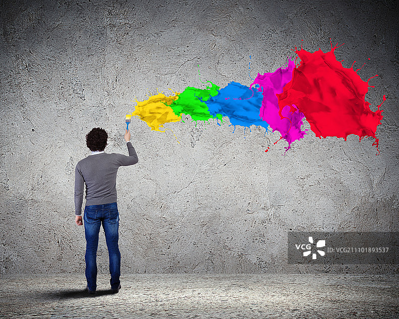 年轻男人和色彩飞溅。年轻男人在背景上喷洒彩色油漆图片素材