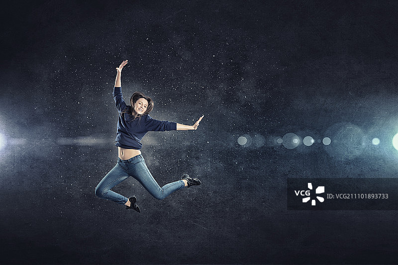 聚光灯下跳跃的年轻女舞者图片素材