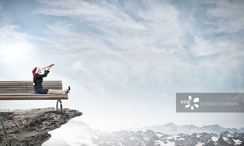 她期待着圣诞节。身穿正装、头戴圣诞帽的女人正在用单筒望远镜观察图片素材