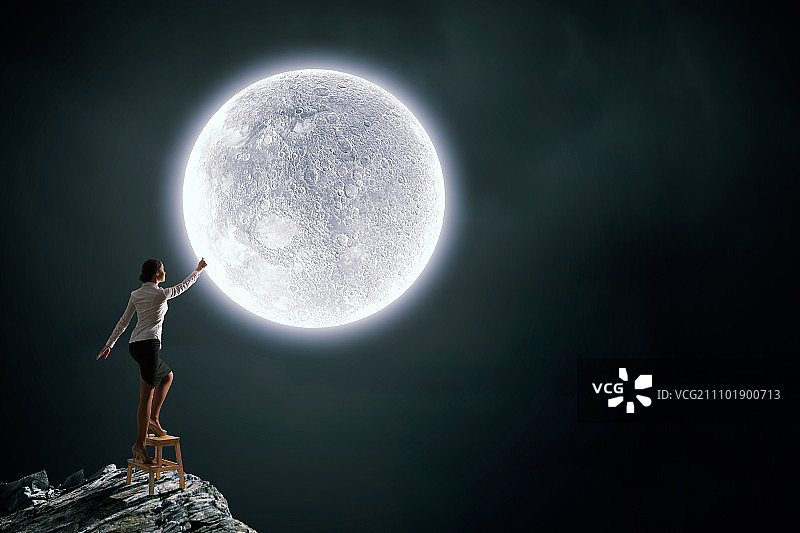 女人举起手。女商人站在椅子上，伸手触摸月亮图片素材