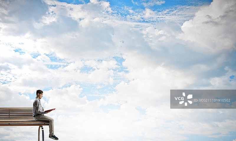 书籍让你脱颖而出：坐在木凳上，手捧书本的休闲年轻人图片素材