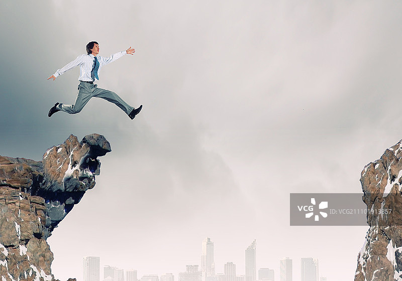 勇敢的商人。身穿西装的年轻商人跳过山间图片素材