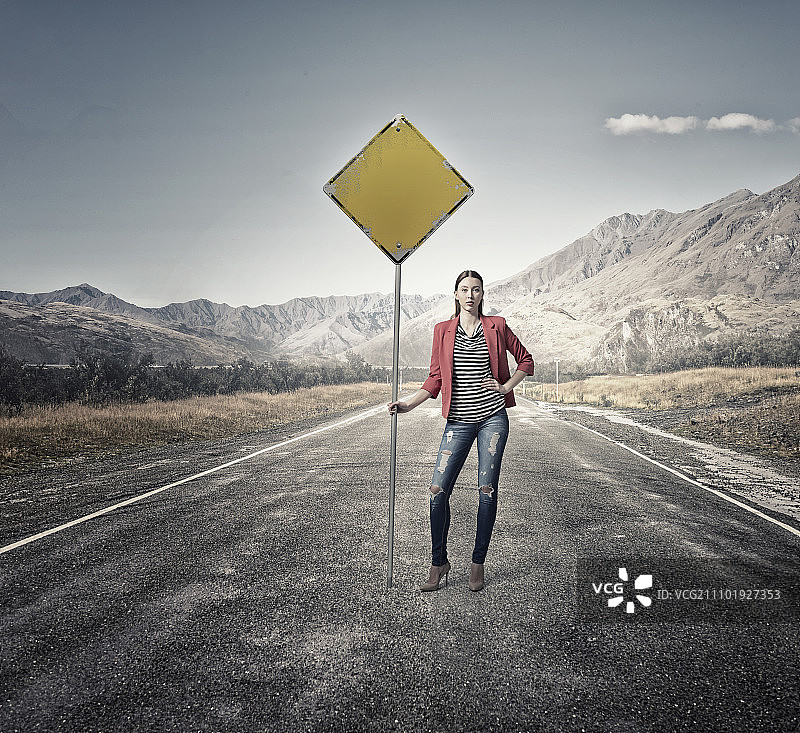 在沥青路上穿着红色外套的年轻漂亮女孩展示路标图片素材
