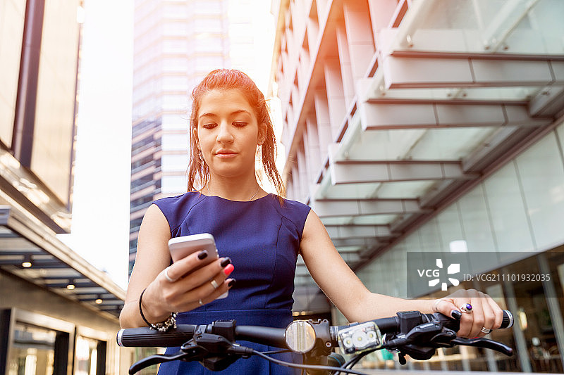 年轻女人骑自行车通勤，穿着商务装，拿着手机图片素材