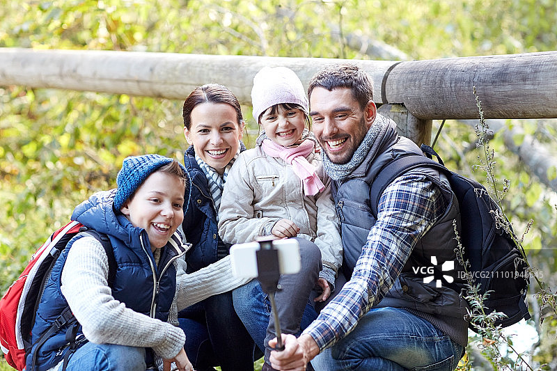 旅行旅游徒步科技：快乐的家人用智能手机和自拍杆在树林里拍照图片素材