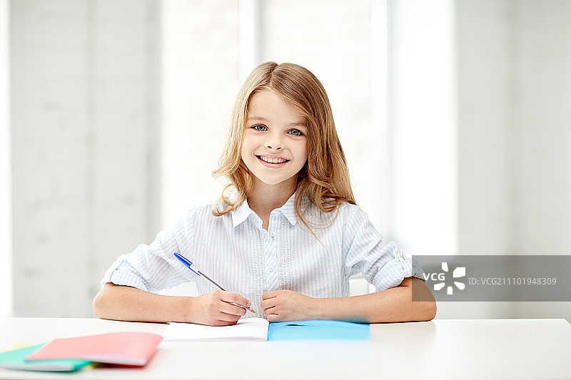 小学教育学习概念：快乐微笑的女孩，拿着笔记本和笔图片素材