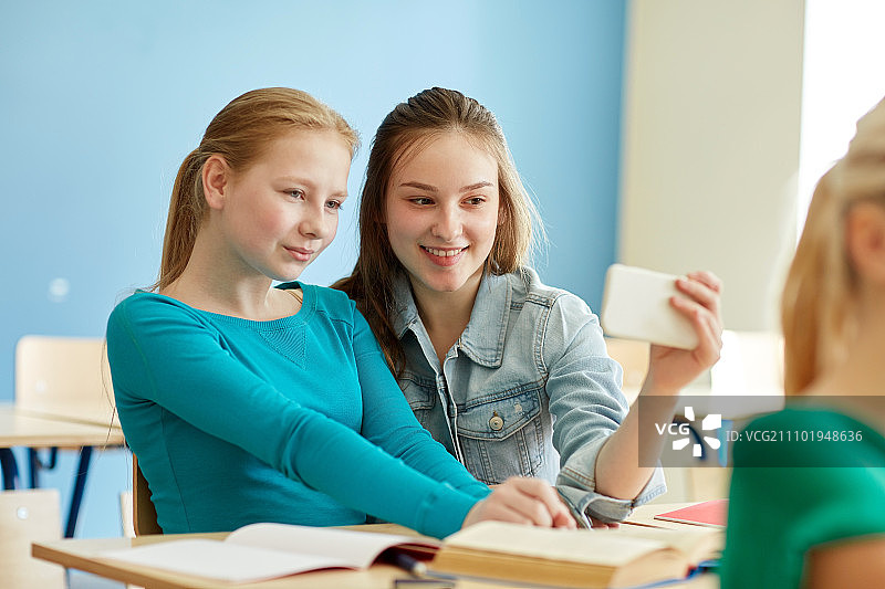 教育，学习，科技，友谊理念 - 女学生在课堂上用智能手机自拍图片素材