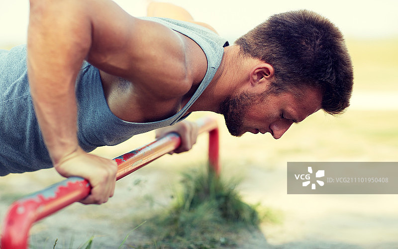 健身运动训练生活方式概念：年轻男子在户外单杠上做俯卧撑图片素材