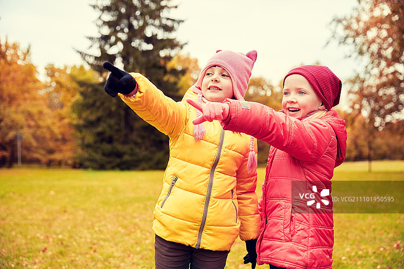 秋季，童年，休闲概念：两个快乐的小女孩在秋季公园里指着什么图片素材