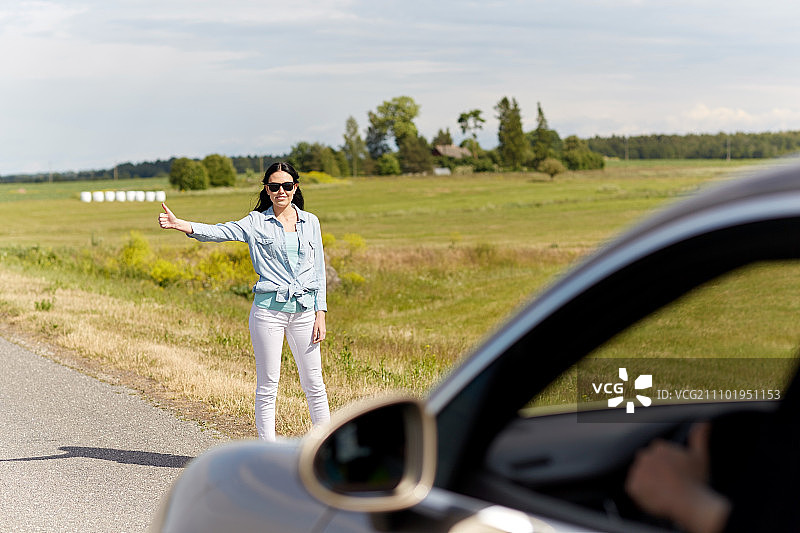 乡村公路搭便车旅行：女子竖起大拇指拦车图片素材